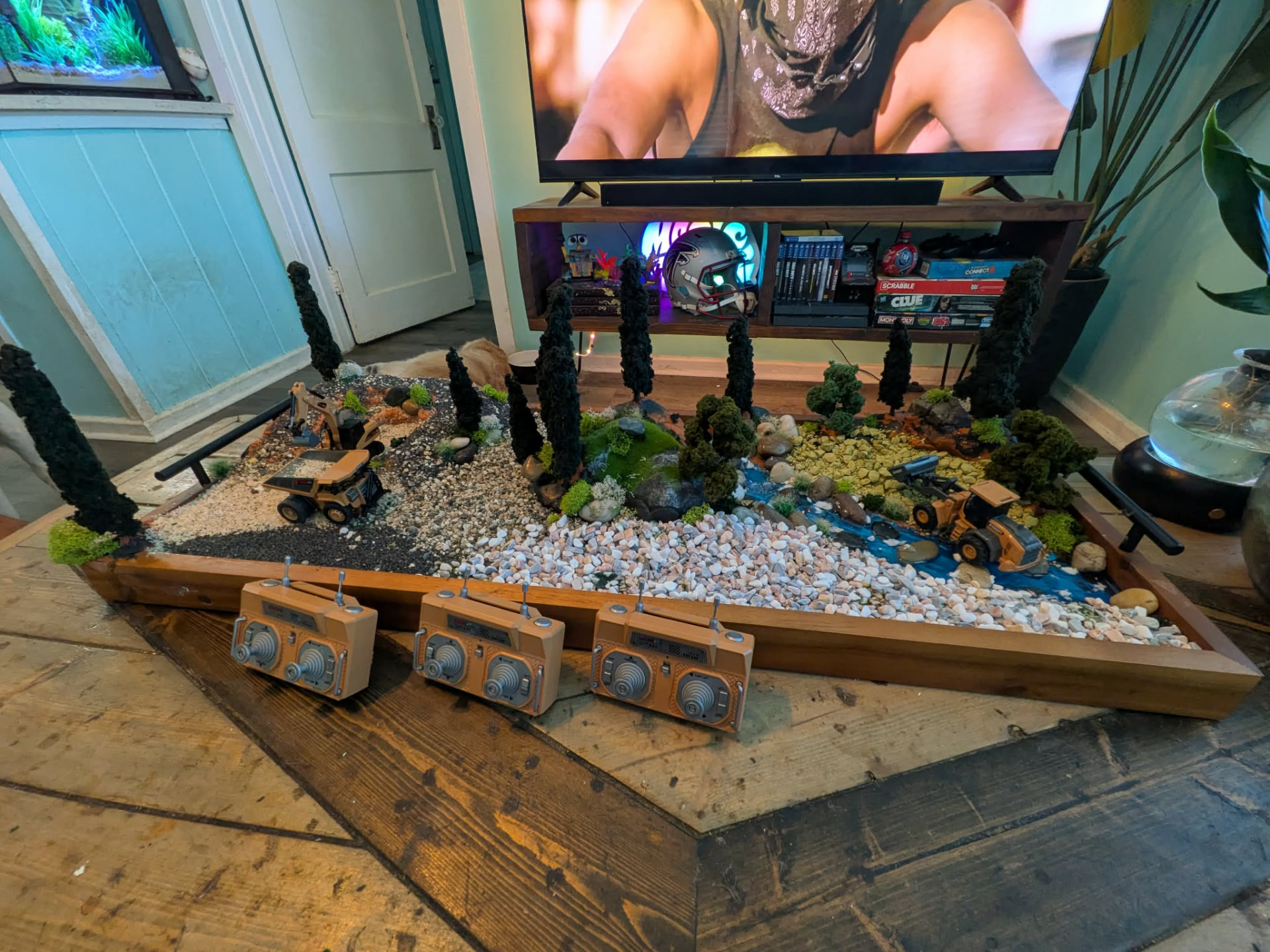 The same Grand Dig terrain board set up in a living room with three RC controllers