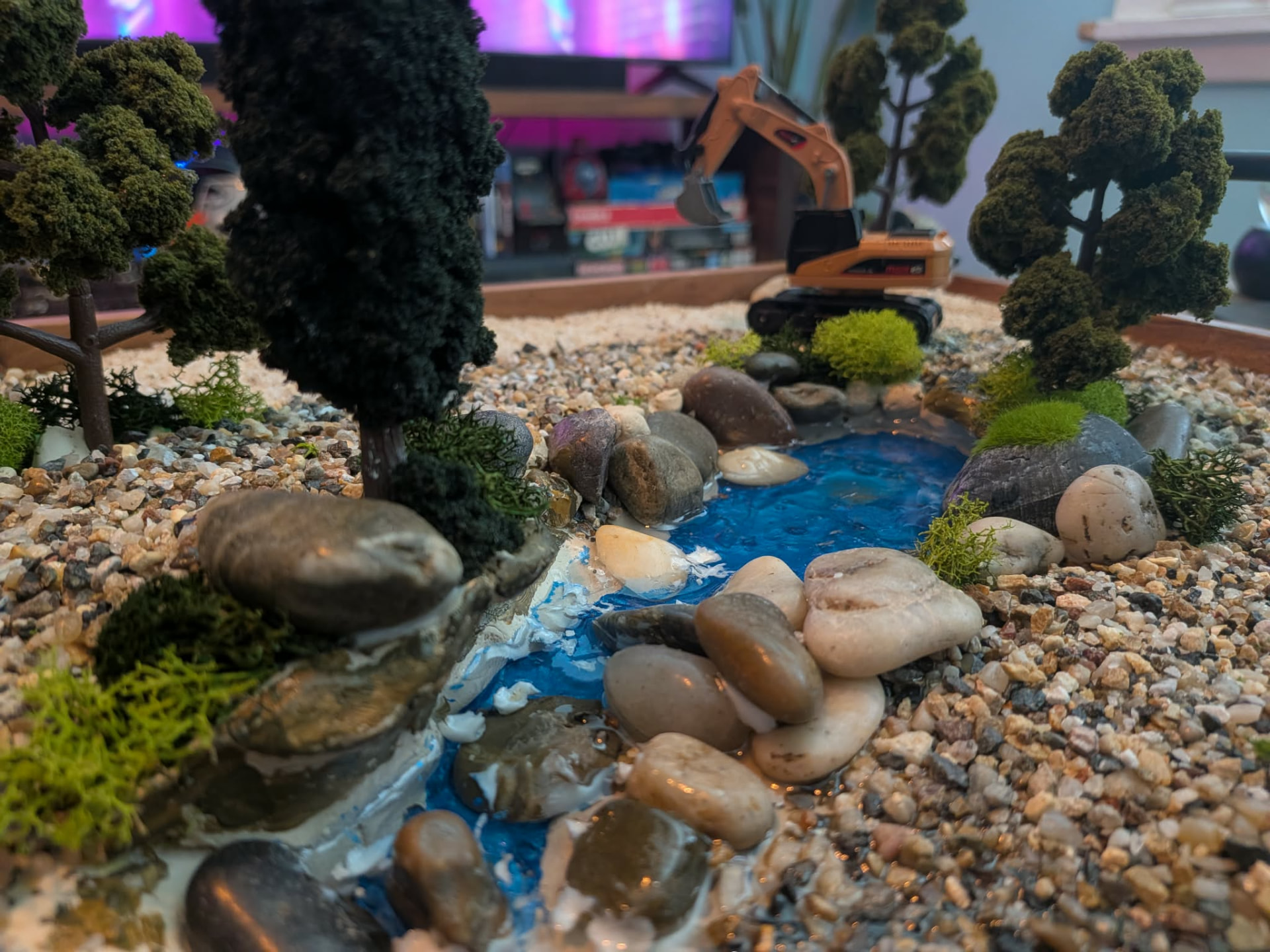 Close-up of hand-poured stream with river rock, moss and RC excavator behind