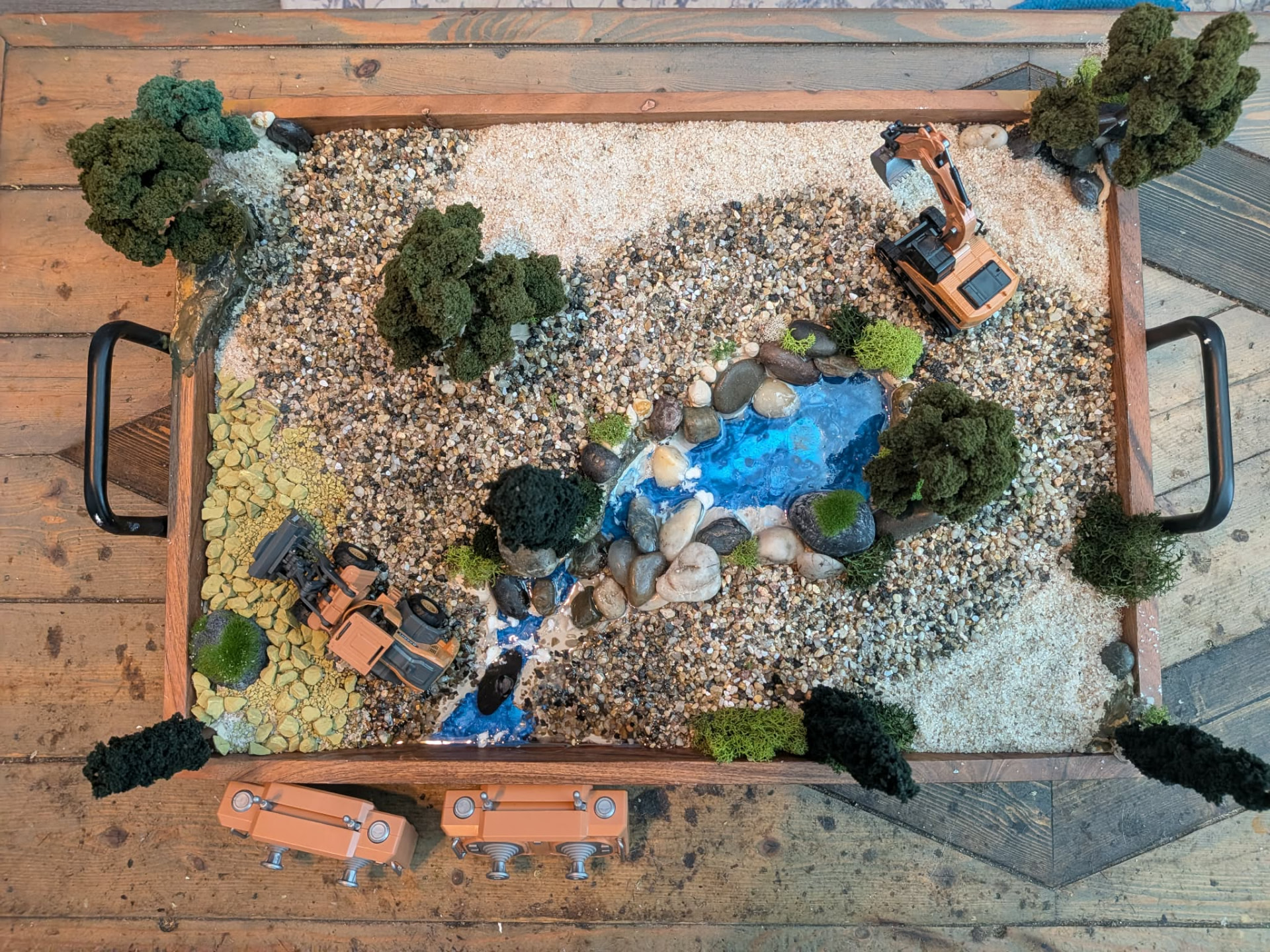 Top-down photo of a finished RC dig site with stream, gravel haul area and RC excavator