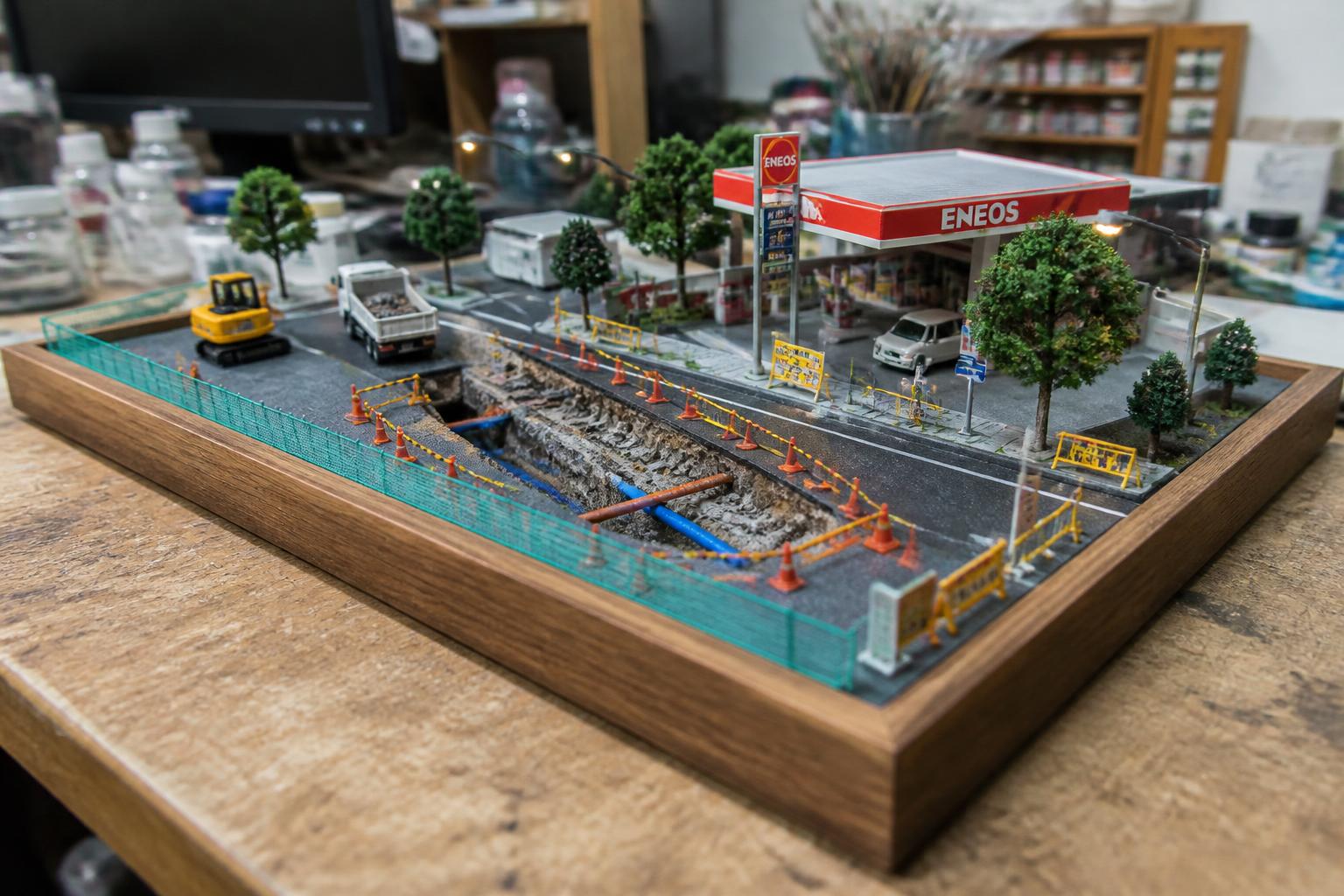 Miniature city street dig site with an open utility trench, corner gas station and lit LED lampposts