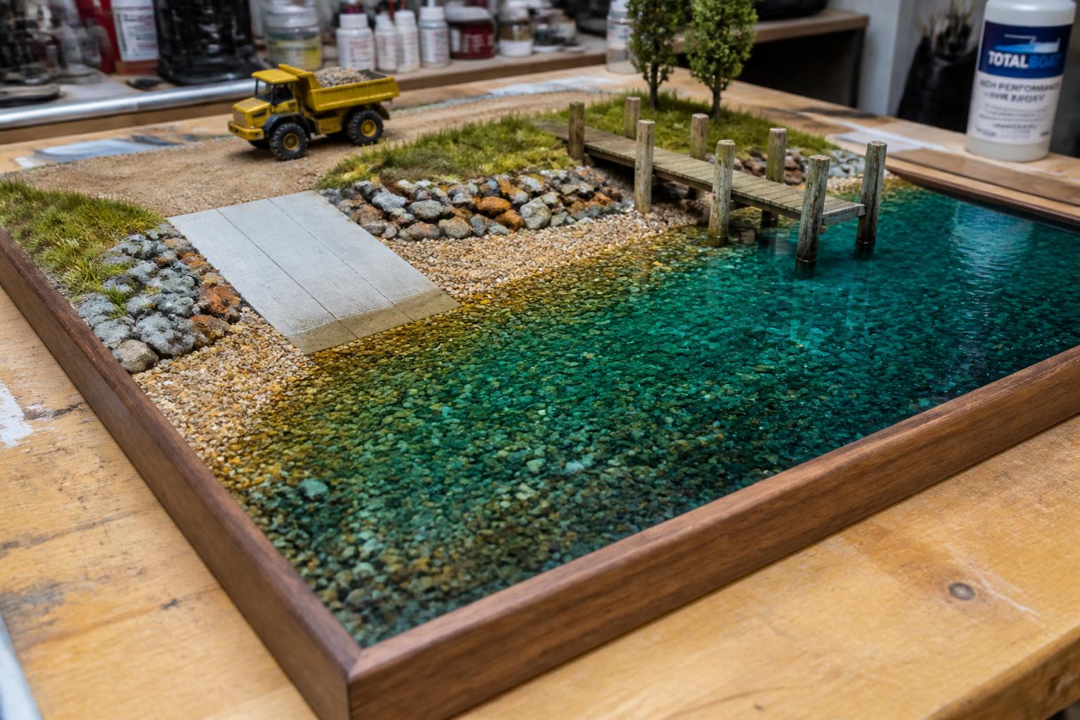 Miniature lakeside scene with turquoise epoxy water, gravel beach, concrete boat ramp and dump truck